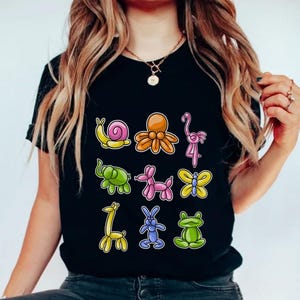 May include: A black t-shirt with a colorful graphic of balloon animals. The animals include a snail, octopus, flamingo, elephant, giraffe, butterfly, rabbit, and frog.