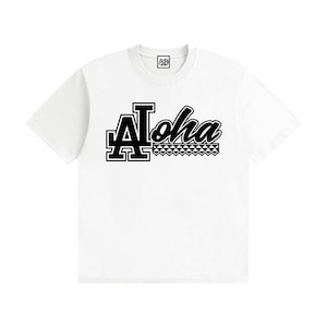May include: A white short-sleeve t-shirt featuring a black graphic on the chest. The graphic displays the word Aloha in a stylized font, with the letter A designed in a block style and a geometric pattern underneath the letters loha.