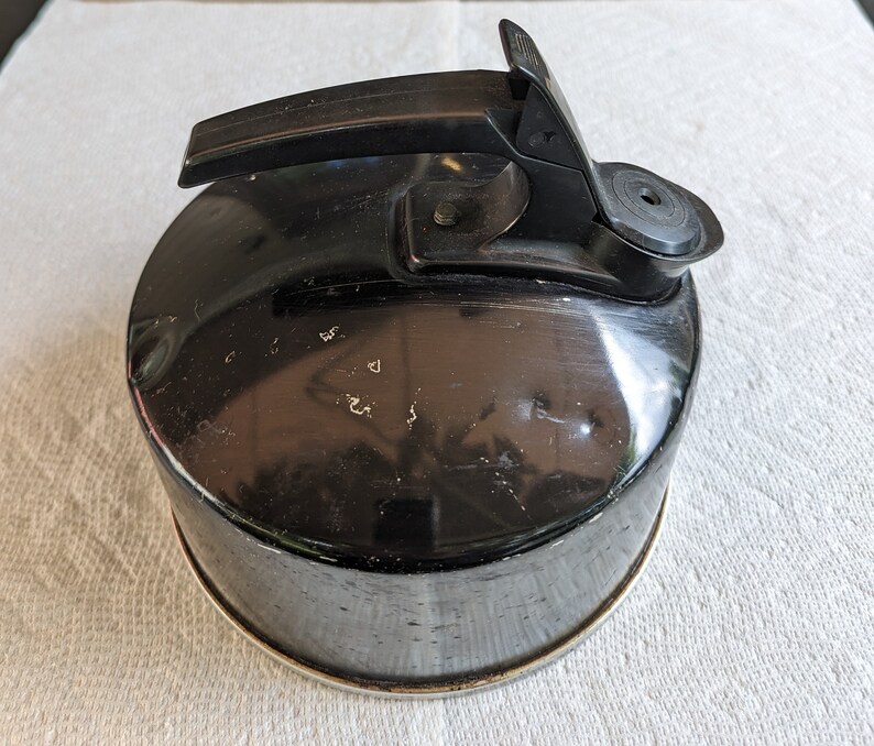 K&ouml;nnte beinhalten: Schwarzer Metall-Wasserkocher mit schwarzem Griff und Ausguss. Der Wasserkocher hat ein abgenutztes, altes Aussehen.