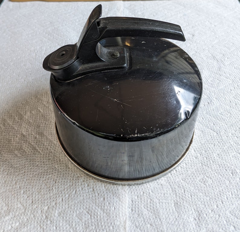 K&ouml;nnte beinhalten: Ein schwarzer Metall-Wasserkocher mit einem schwarzen Kunststoffgriff. Der Wasserkocher hat eine gl&auml;nzende Oberfl&auml;che und einen kleinen Ausguss.