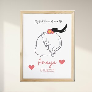 May include: A white framed print with a black and white illustration of a baby girl with a single strand of hair tied with a pink flower. The text "My first strand of hair" is above the illustration and the name "Amaya" and the date "07.08.2021" are below the illustration.