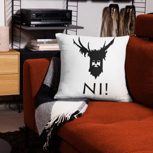 May include: White throw pillow with a black silhouette of a stag head with a crown and the word "NI!" printed below.