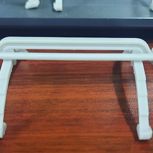 May include: White plastic model of a suspension bridge with two curved supports and a straight beam connecting them.