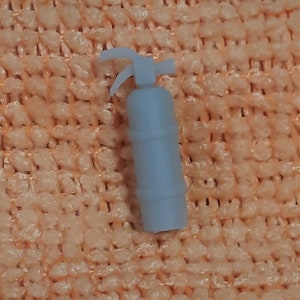 May include: A small, white plastic fire extinguisher with a red handle. The extinguisher is about 4 inches tall and has a nozzle on the top.