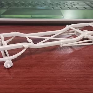 May include: A white plastic model car chassis, featuring a detailed frame with suspension components. The model is designed for hobbyists and enthusiasts interested in automotive design and construction. The chassis is approximately 10 inches long.