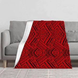 May include: A red and black patterned blanket draped over a gray sofa. The blanket features a repeating geometric design with tribal-inspired motifs. The underside of the blanket is white.