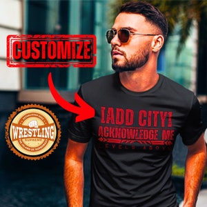 May include: Black t-shirt with red text that reads "I ADD CITY! ACKNOWLEDGE ME LEVELS ABOVE". The shirt has a distressed look. A brown and orange circular logo with the text "ESTABLISHED 2023 WRESTLING SUPREME THE ISLAND OF SUPREMACY" is in the lower left corner of the image. The text "CUSTOMIZE" is in a red stamp in the upper left corner of the image.