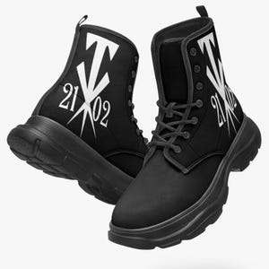 Może przedstawiać: Czarne buty bojowe z białym wzorem graficznym po bokach. Buty mają sznurowane zapięcie i grubą, masywną podeszwę. Grafika zawiera liczby "21 02" i stylizowaną literę "T".