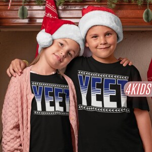 May include: Two children wearing black t-shirts with a white and blue "YEET" graphic. The shirts have a white and gray chevron pattern around the graphic. The children are wearing Santa hats and smiling.