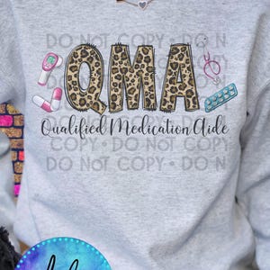 May include: A gray sweatshirt with the text "QMA Qualified Medication Aide" in black and leopard print letters. The letters are surrounded by medical icons, including a stethoscope, thermometer, and pills.