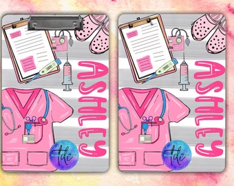 May include: A pink and gray clipboard with a white background. The clipboard has a white paper with lines on it, a pink stethoscope, a pink scrub top, a pink syringe, a pink thermometer, a pink IV bag, a pink pair of clogs, and the name "Ashley" written in pink letters. The clipboard has a gray and white striped background.