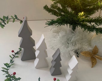 Puede incluir: Una colección de árboles de Navidad decorativos en varios tamaños y tonos de gris y blanco. Un pequeño árbol de Navidad artificial con luces de hadas está en el fondo, junto con una guirnalda de acebo con bayas rojas y un acento decorativo dorado.