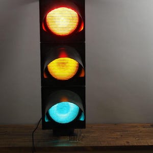 May include: A black traffic light with three lights. The top light is red, the middle light is yellow, and the bottom light is green.