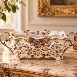 May include: A rectangular ceramic planter with a scalloped rim, featuring a cream-coloured base decorated with a colourful floral pattern. The vessel includes two ornate gold-toned metal handles and a central gold-toned floral embellishment.
