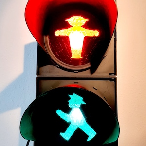May include: A red and green traffic light with a pedestrian symbol. The red light is on, and the green light is off. The pedestrian symbol is a stick figure with outstretched arms.
