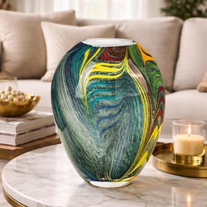Peut inclure: Un vase décoratif en verre de forme large et arrondie. Le vase présente un motif tourbillonnant de couleurs bleues, vertes, jaunes et rouges. Le vase est posé sur une table à plateau en marbre avec une base en métal doré.