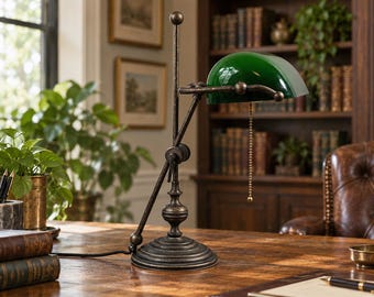 Könnte beinhalten: Eine Bankerlampe mit einem dunkel bronzefarbenen Metallsockel und einem halbzylindrischen smaragdgrünen Glasschirm. Die Lampe verfügt über einen verstellbaren Arm, einen runden, gestuften Sockel und einen goldenen Zugschalter am Schirm.