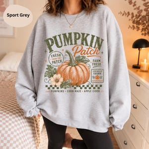 Könnte beinhalten: Ein sportgrauer Rundhals-Pullover mit einer Grafik eines großen orangefarbenen Kürbisses mit grünen Blättern. Der Text lautet PUMPKIN Patch, FRESH FROM THE PATCH, FARM FRESH, LOCALLY GROWN, AUTUMN PICKED, PUMPKINS, CORN MAZE und APPLE CIDER.