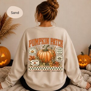 Könnte beinhalten: Ein sandfarbenes Sweatshirt mit Rundhalsausschnitt und einem großen Rückendruck mit dem Text PUMPKIN PATCH, einer zentralen orangefarbenen Kürbisillustration, Herbstblättern sowie kleinen runden Etiketten mit FRESH FROM THE PATCH und FARM FRESH.