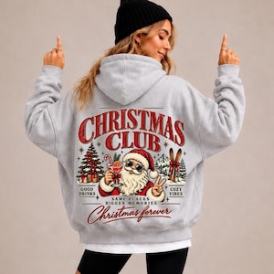 Könnte beinhalten: Ein hellgrauer Kapuzenpullover mit einem Rückendruck, der den roten Schriftzug "CHRISTMAS CLUB" zeigt. Das Motiv enthält einen Weihnachtsmann mit Sonnenbrille und Cocktail, einen Tannenbaum, Skier sowie die Texte "GOOD DRINKS", "COZY VIBES", "SAME PLACES BIGGER MEMORIES" und "Christmas forever".