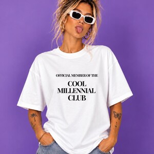 Könnte beinhalten: Ein weißes T-Shirt mit kurzen Ärmeln und dem schwarzen Schriftzug "OFFICIAL MEMBER OF THE COOL MILLENNIAL CLUB" auf der Vorderseite. Das Shirt hat einen Rundhalsausschnitt und eine lockere Passform aus schlichtem, weißem Stoff mit schwarzer Schrift.