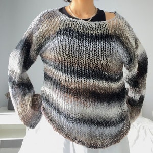 Może przedstawiać: Sweter w paski, luźny, w jasnobrązowym, szarym i czarnym kolorze. Sweter ma lekko otwarty dekolt i luźny krój.