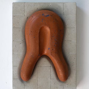 Può includere: Scultura astratta in terracotta, con un elemento centrale a forma di U e due curve verso il basso, montata su una base quadrata in cemento grigio piastrellato. La terracotta presenta macchie di vernice blu. Un'opera d'arte moderna.
