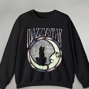 Peut inclure: Sweat-shirt noir avec un imprimé graphique d'un chat noir assis sur un croissant de lune avec un visage. Le texte "Mazzystar" est imprimé au-dessus du graphique.