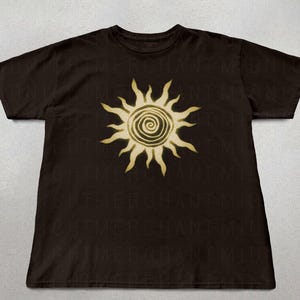 May include: A black t-shirt with a gold sun graphic. The sun has a spiral design in the center.