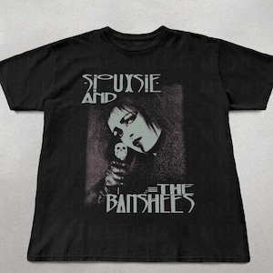 May include: Black t-shirt featuring a grayscale image of Siouxsie Sioux holding a skull, with the band name "Siouxsie and the Banshees" printed in white. The shirt has a crew neck and short sleeves.