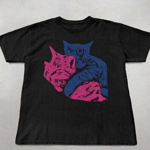 May include: Black t-shirt with a graphic of two cats, one pink and one blue, in an embrace. The design is centrally placed. The shirt is made of a soft material.