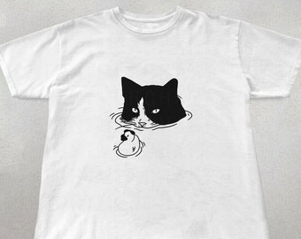 Könnte beinhalten: Ein weißes T-Shirt mit einer schwarz-weißen Illustration eines Katzenkopfes, der aus dem Wasser schaut, und einem kleinen Entenküken, das daneben schwimmt.