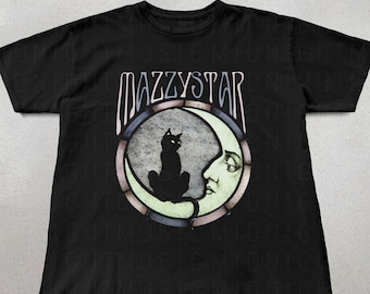 以下が含まれることがあります： 黒いTシャツに、顔のある三日月の上に座っている黒い猫のグラフィックがプリントされています。グラフィックはステンドグラス風で、ピンク、ブルー、グリーンの色が使われています。グラフィックの上に「Mazzystar」という文字があります。