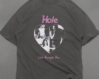 May include: A dark gray t-shirt with a pink heart graphic featuring black and white photos of a band. The text "Hole" and "Live Through This" are printed on the shirt.