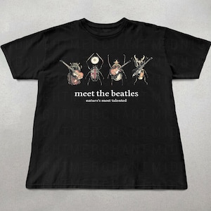 Op de afbeelding: Een zwart t-shirt met een afbeelding van vier kevers die muziekinstrumenten bespelen. Onder de insecten staat de tekst "meet the beatles" in een groter lettertype en "nature's most talented" in een kleiner lettertype op de borst.
