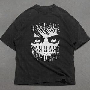 May include: Black t-shirt with a white graphic of a face with eyes and the word "BAUHAUS" repeated multiple times.