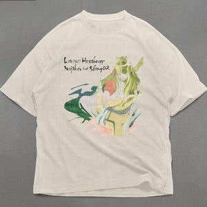 May include: Cream-colored t-shirt featuring a colorful illustration of a figure with green hair and a flowing green cape. The text "Luv(sic) Hexalogy Nujabes feat Shing02" is printed above the illustration. The word "PREMIUM" is in the top left corner.