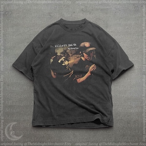 May include: A charcoal gray short-sleeve t-shirt featuring a graphic print of Elliott Smith with the text Elliott Smith either/or. The shirt has a crew neckline and a relaxed fit, showcasing a vintage-style faded aesthetic on the fabric.