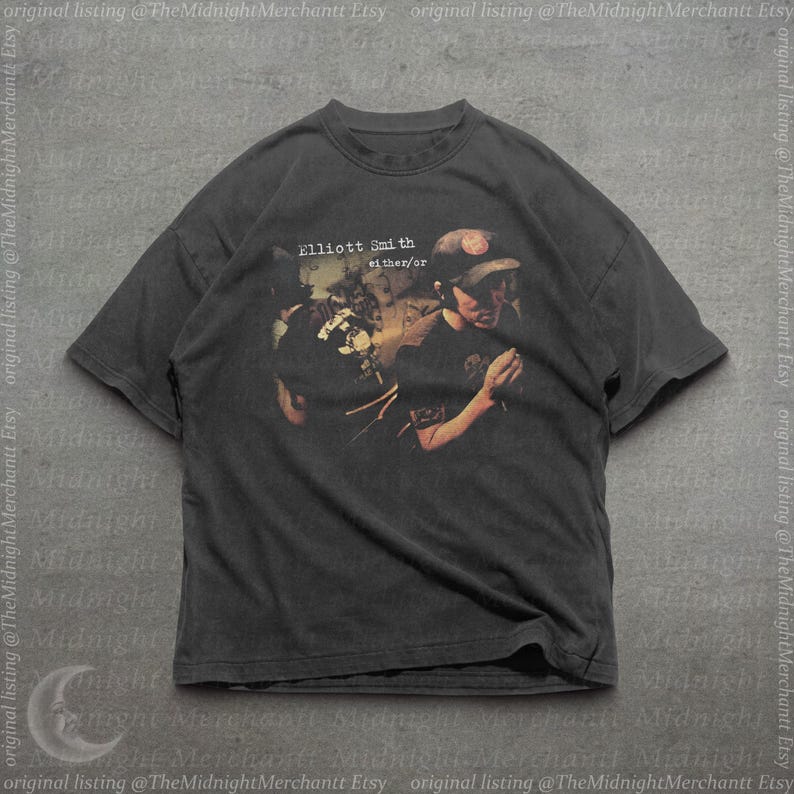 May include: A charcoal gray short-sleeve t-shirt featuring a graphic print of Elliott Smith with the text Elliott Smith either/or. The shirt has a crew neckline and a relaxed fit, showcasing a vintage-style faded aesthetic on the fabric.