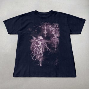 May include: Navy blue t-shirt featuring a detailed, gothic-inspired illustration of a winged figure with intricate details in shades of purple and white. The design has a dark, ethereal aesthetic.