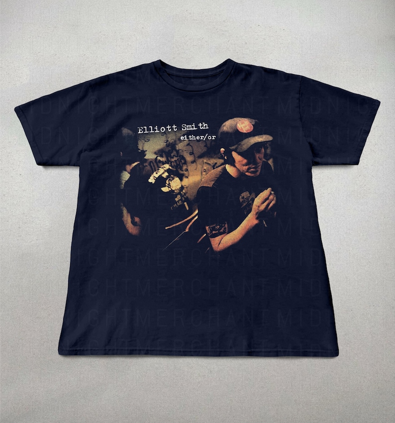 May include: Navy blue t-shirt with the text "Elliott Smith either/or" and a faded image of a person wearing a baseball cap. The graphic design is in shades of brown and black.