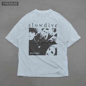 Puede incluir: Camiseta blanca con una imagen en blanco y negro de la banda Slowdive. El nombre de la banda est&aacute; impreso encima de la imagen, y el t&iacute;tulo del &aacute;lbum "souvlaki" est&aacute; impreso debajo. La camiseta tiene cuello redondo y mangas cortas.