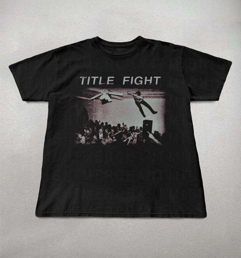 May include: Black t-shirt featuring a grayscale graphic of a live performance with the band name "TITLE FIGHT" in white block letters above the image. The graphic shows a person jumping from a stage.