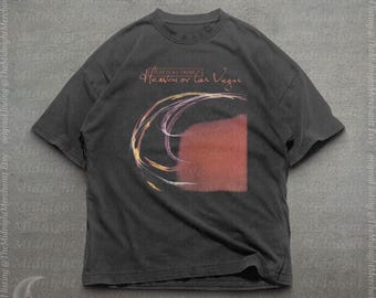 May include: A charcoal gray short-sleeve t-shirt featuring a graphic print of the Cocteau Twins album Heaven or Las Vegas. The design includes abstract swirling lines in shades of yellow and purple alongside a solid reddish-brown rectangular shape.