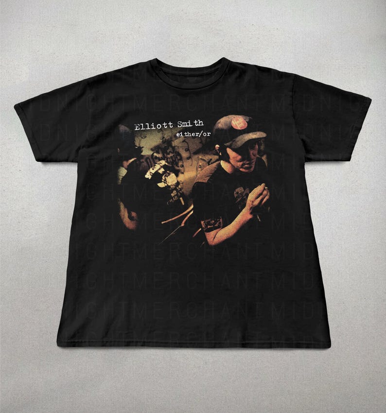 May include: Black t-shirt with the text "Elliott Smith either/or" and a faded image of a person in a baseball cap. The design has a vintage, slightly worn appearance.