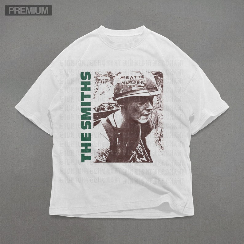Puede incluir: Camiseta blanca con un estampado verde y marr&oacute;n de una persona con un casco con el texto "Meat is Murder". El texto "The Smiths" est&aacute; impreso verticalmente en el lado izquierdo de la camiseta.