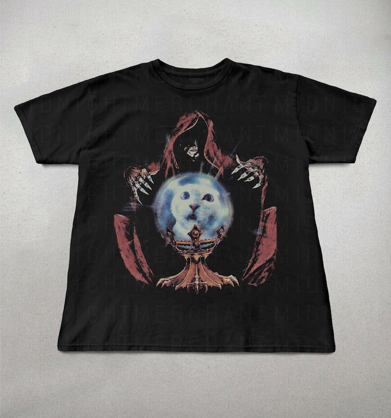 May include: Black t-shirt featuring a graphic of a hooded figure with clawed hands holding a crystal ball with a cat's face inside. The crystal ball sits on a decorative stand. The design is in shades of red, blue, and gold.