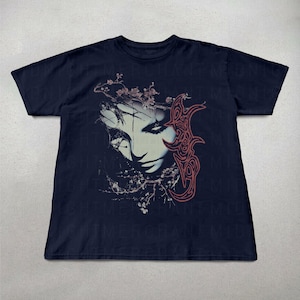 K&ouml;nnte beinhalten: Marineblaues T-Shirt mit einem grafischen Aufdruck eines stilisierten Frauengesichts, floralen Elementen und einem abstrakten Design in Rosa und Wei&szlig;. Das Design hat ein gotisches Thema.
