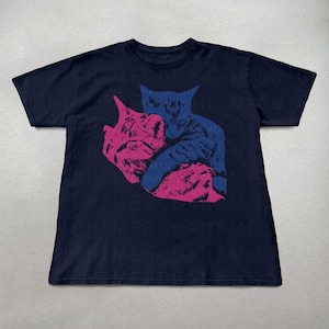 Pu&ograve; includere: T-shirt blu navy con una grafica di due gatti, uno rosa e uno blu, che si abbracciano. Il design &egrave; un'illustrazione stilizzata. La maglietta ha un girocollo e maniche corte.