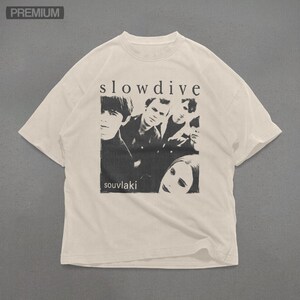 Puede incluir: Camiseta color crema con una imagen en blanco y negro de una banda. El texto "slowdive" est&aacute; arriba y "souvlaki" abajo. La camiseta tiene cuello redondo y mangas cortas.
